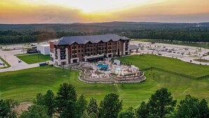 A multi-story hotel with a swimming pool, surrounded by green lawns and a parking lot. - Choctaw Landing Casino & Resort, Trademark Collection by Wyndham (Hochatown)