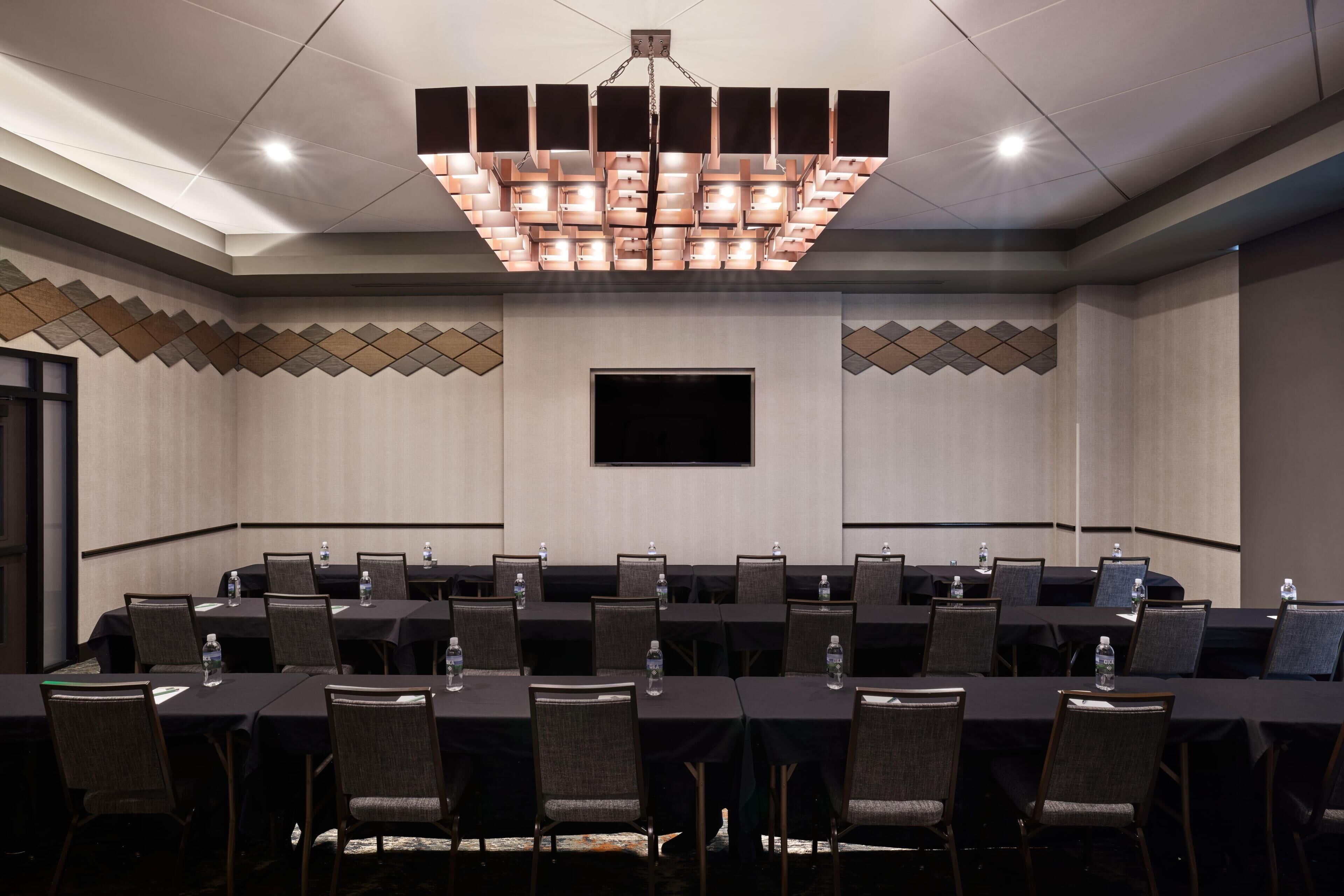 A conference room with a long table, chairs, a flat-screen TV, and a modern chandelier.