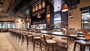 A bar area with a long counter, multiple stools, and hanging pendant lights. - Choctaw Landing Casino & Resort, Trademark Collection by Wyndham (Hochatown)
