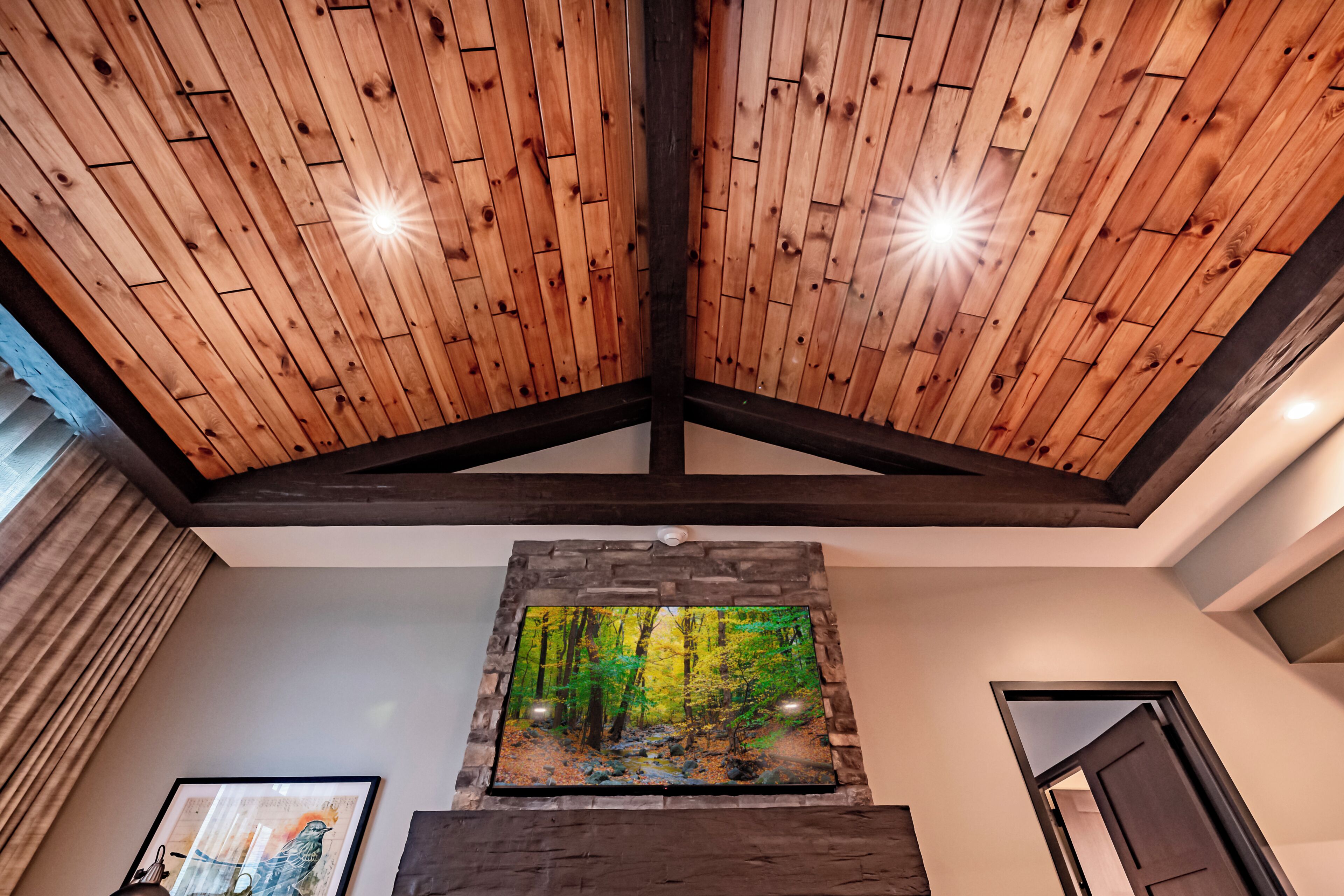 A room with a wooden ceiling, a framed painting of a forest, and a door.