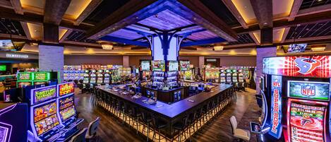 A casino with multiple gaming machines, a central bar area, and a high ceiling with exposed beams.