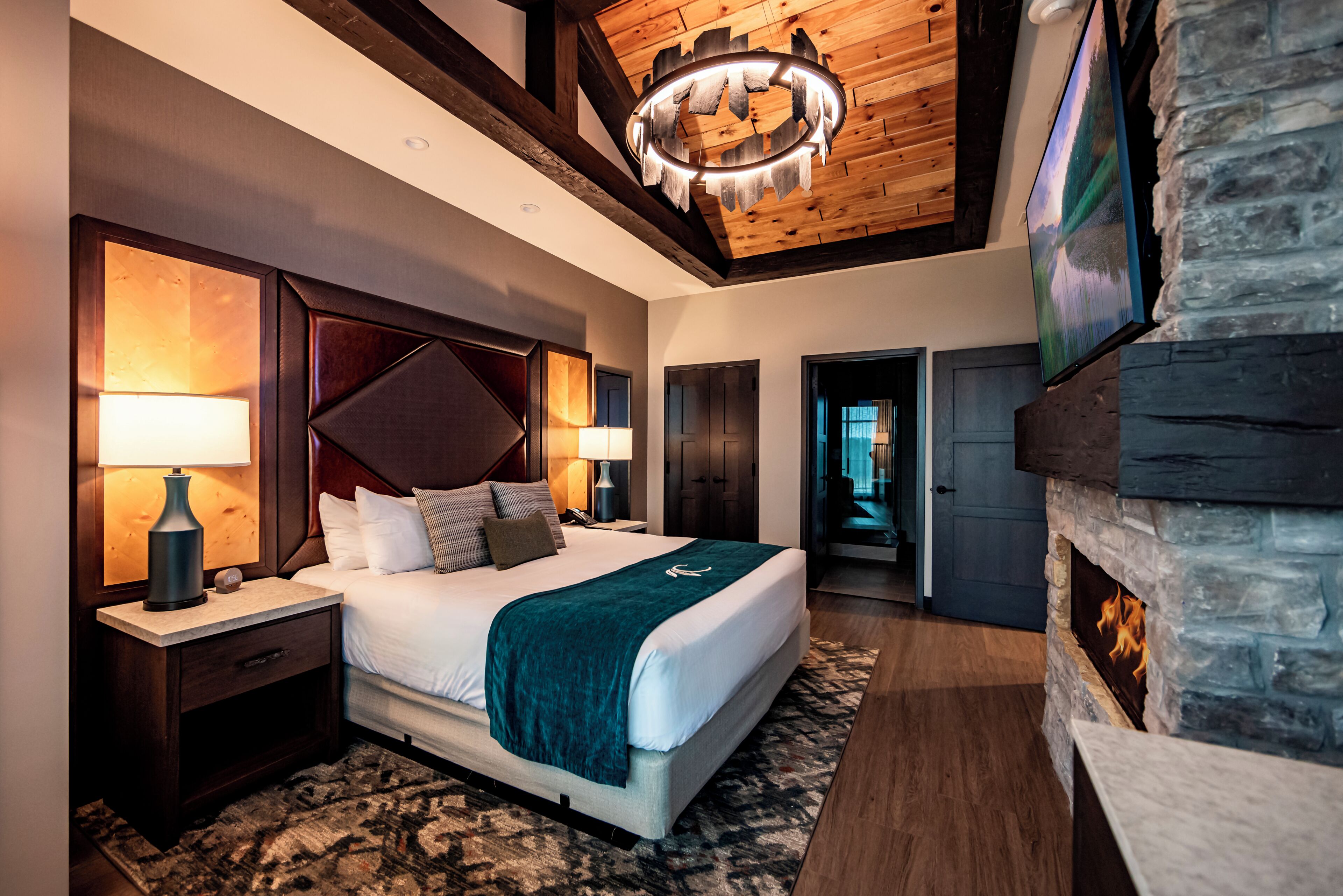 A modern bedroom with a large bed, a stone fireplace, and a television mounted on the wall.
