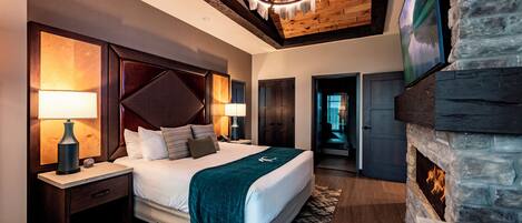 A modern bedroom with a large bed, a stone fireplace, and a television mounted on the wall.
