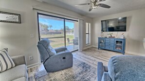 Ein Wohnzimmer mit grauem Sofa, einem blauen Schrank, einem Deckenventilator und einem großen Fernseher an der Wand.