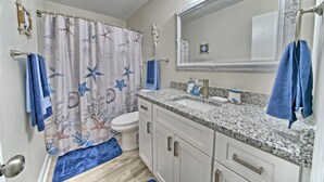 Ein Badezimmer mit Duschvorhang mit Meereslebewesen, Toilette, Waschbecken mit Spiegel darüber und einer blauen Badematte.