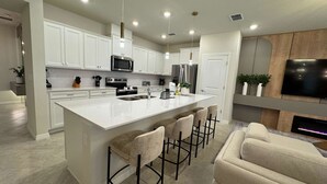 A modern kitchen with white cabinets, stainless steel appliances, and a large island with bar stools. - Family Friendly 5Bd Near Disney Windsor Cay 16136 (Clermont)