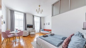 En moderne stue med sofa, spisebord med stole, fjernsyn og seng med puder.