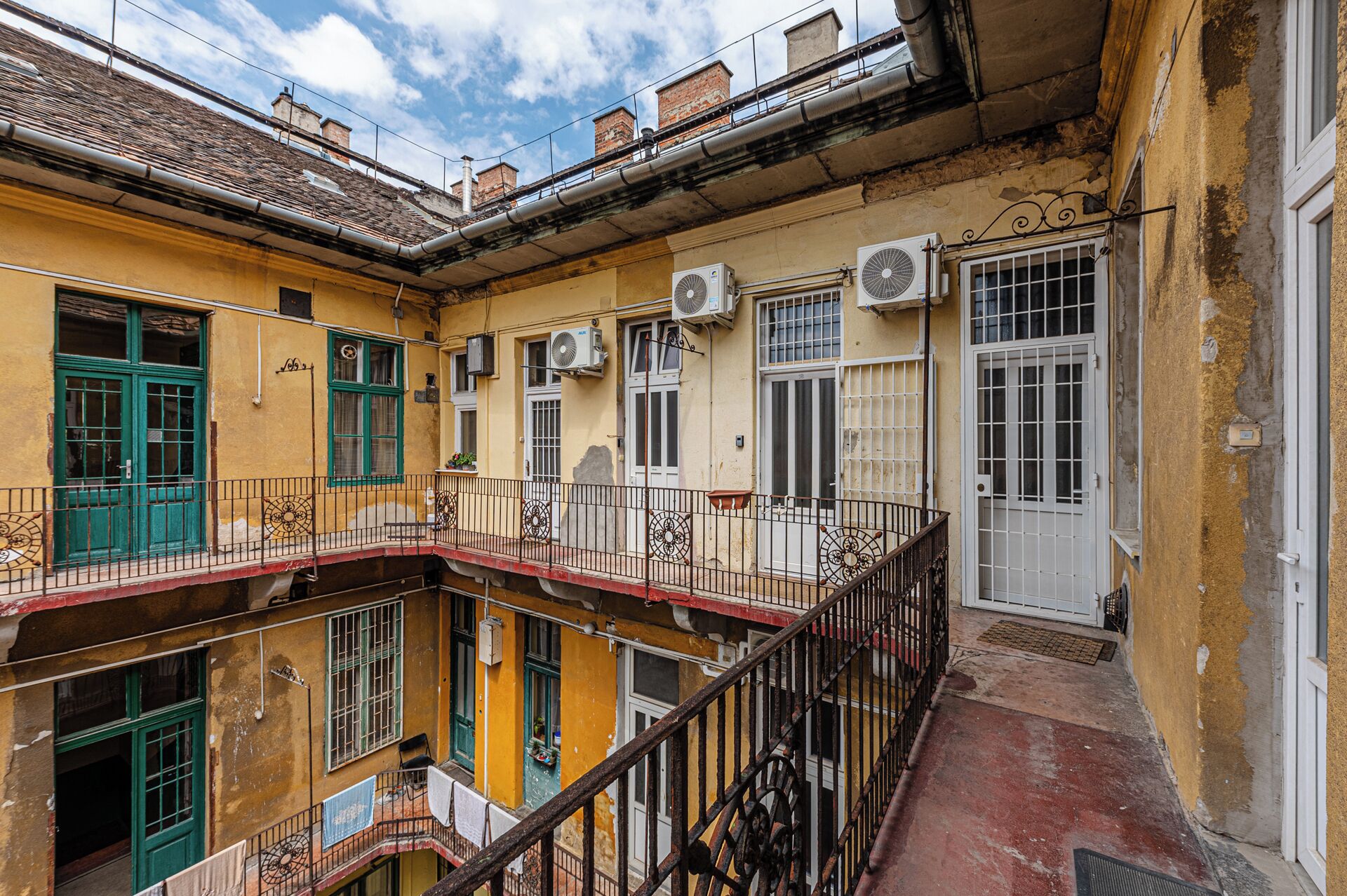 Um edifício com várias andares, varandas, aparelhos de ar condicionado e telhado de telhas vermelhas.