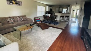 A spacious living room with a sofa, coffee table, and a dining area with chairs. - Spacious 4-bedroom house in fantastic Buda with WiFi, game /fitness room& more! (Buda)