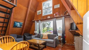 Interior acogedor de una cabaña con escalera de madera, un conjunto de sofás, una mesa de comedor y una zona de cocina.