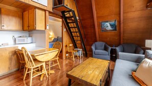 Un espacio habitable compacto con cocina, comedor y zona de estar. Cuenta con interior de madera, una escalera y un cuadro enmarcado en la pared.