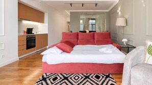 A bedroom with a large bed, a kitchenette, a mirror, and a lamp.