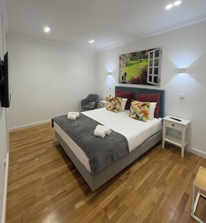 A bedroom with a bed, a chair, a nightstand, a painting, and a TV. - Luxury stay premium Douro river & sunset views (porto)
