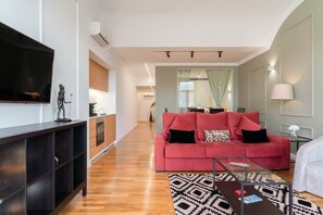 A modern living room with a red sofa, a glass coffee table, and a TV mounted on the wall.