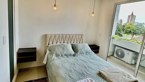 Une chambre moderne avec un lit, des tables de chevet, une fenêtre donnant sur un beau paysage et des lampes suspendues.