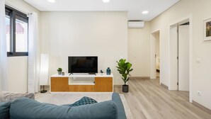 En moderne stue med et fladskærms-tv, et træunderholdningscenter, en potteplante og en blå sofa.