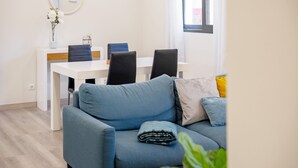 En moderne stue med en blå sofa, et spisebord med stole, en vase med blomster og et vindue med gardiner.