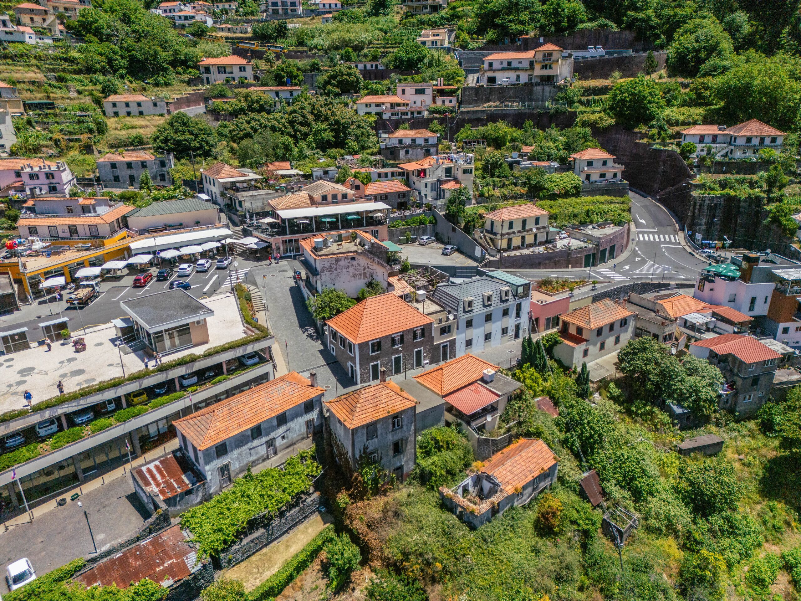 An aerial view of a hillside town with terraced houses, a central square, and a parking area.