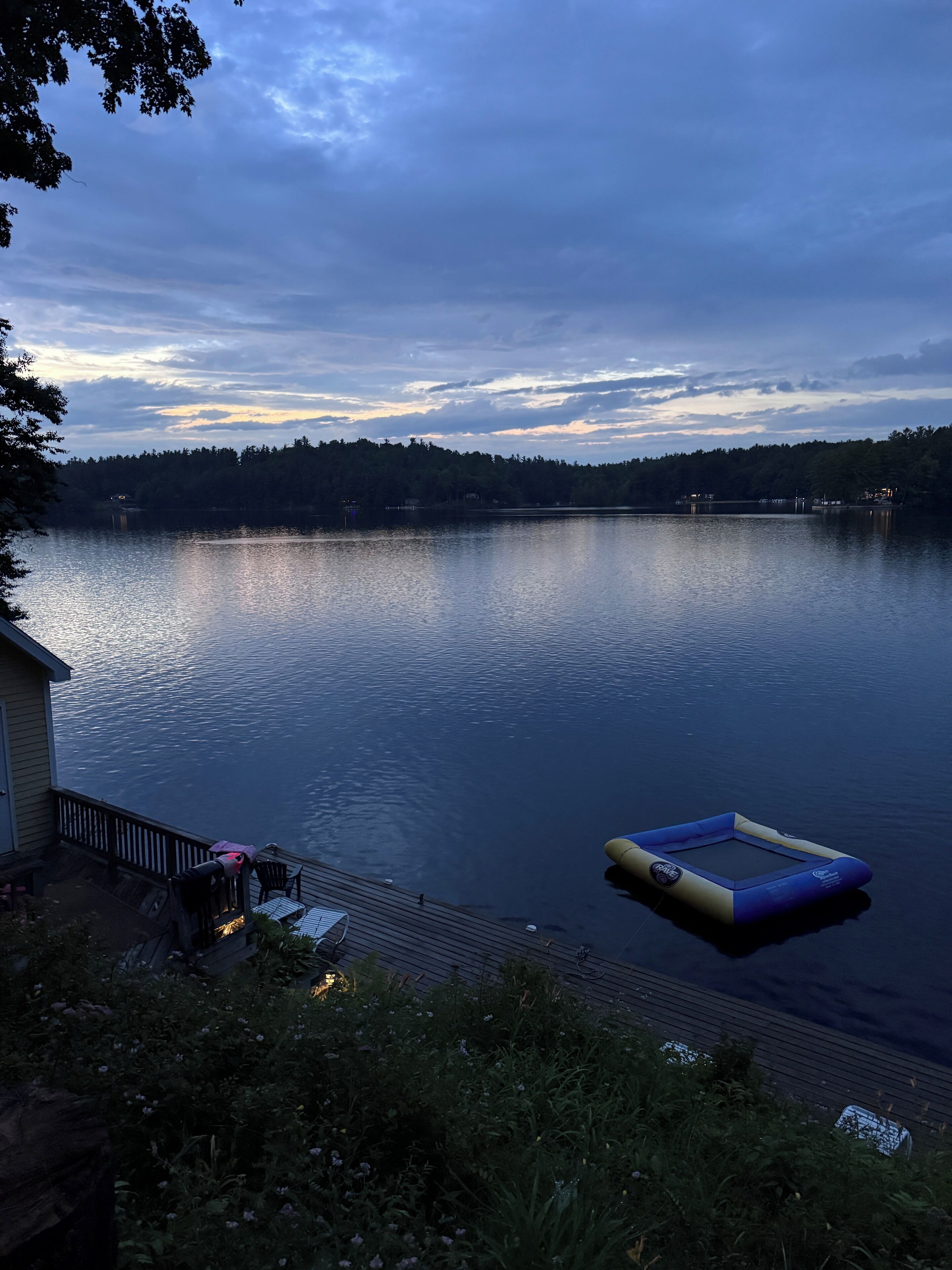 A lakeside view with a dock, a floating platform, and a house with outdoor seating.