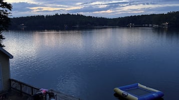 A lakeside view with a dock, a floating platform, and a house with outdoor seating.
