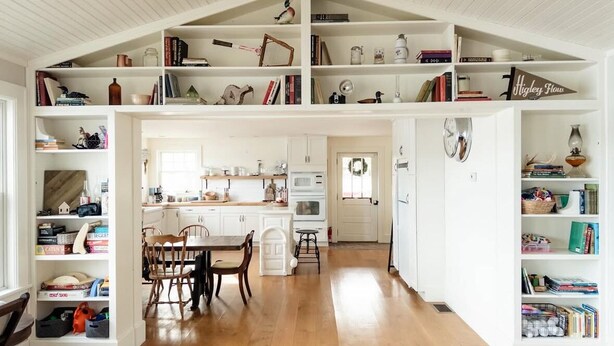 A spacious kitchen with white cabinetry, a dining area with wooden chairs, and a bookshelf filled with books and decorative items. - Hideaway in Higley Flow! (Colton)