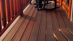 Une personne assise sur une chaise berçante, sur une terrasse en bois, d’où l’on peut admirer un paysage montagneux.