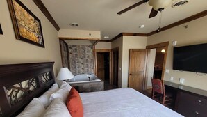Une chambre d’hôtel avec un grand lit, un bureau avec une lampe, un téléviseur fixé au mur et une porte en bois.