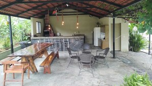 Un espacio de cocina al aire libre con una mesa y sillas de madera, un horno de ladrillo y luces colgantes.