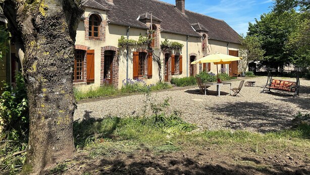 A traditional building with a tiled roof, brick chimneys, and wooden shutters. There is a gravel patio with outdoor furniture and a swing chair. - Entire vacation home in Burgundy style: Longère des Daubénys (Precy-sur-Vrin)