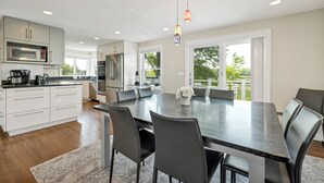 A modern kitchen with white cabinets, stainless steel appliances, and a dining area with a dark table and chairs.
