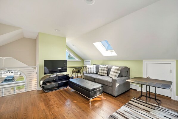 A modern living space with a loft bedroom, a sofa, a TV, and a dining area. - 4 Bedrooms Beach house in beautiful Wells. AC, HOT TUB & SUNSET included (Wells)