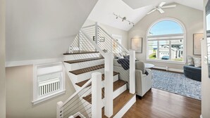 A modern staircase with wooden steps and white railings, leading to a living area with a large window offering a view of the outside.