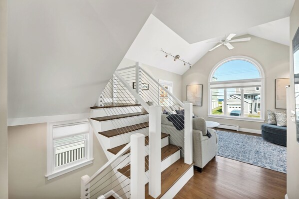 Eine moderne Treppe mit Holzbeschlägen und weißen Geländern, die zu einem Wohnbereich mit einem großen Fenster und Außenblick führt.