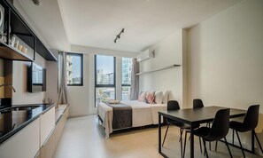 A modern hotel room with a kitchenette, a dining area with a table and chairs, a bed with a view, and large windows. - Modern and Fully Equipped Apartments Just Minutes From Lagoa da Conceicao and the Beach - VTD (Florianópolis)