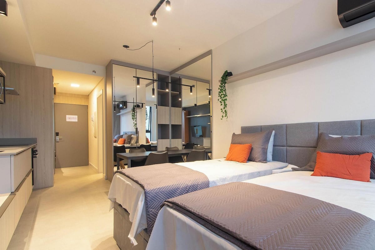A modern hotel room with two beds, a desk, a chair, a mirror, and a plant.