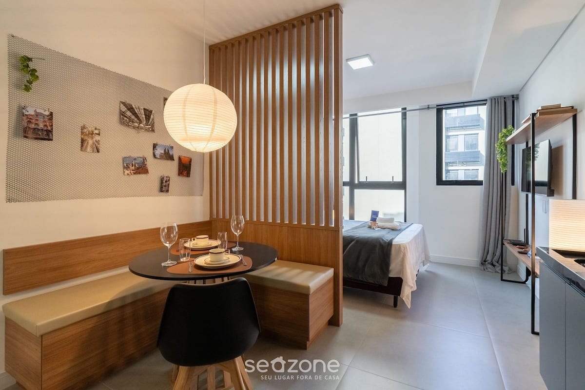A modern hotel room with a dining area, a bed, a kitchenette, and a large window.