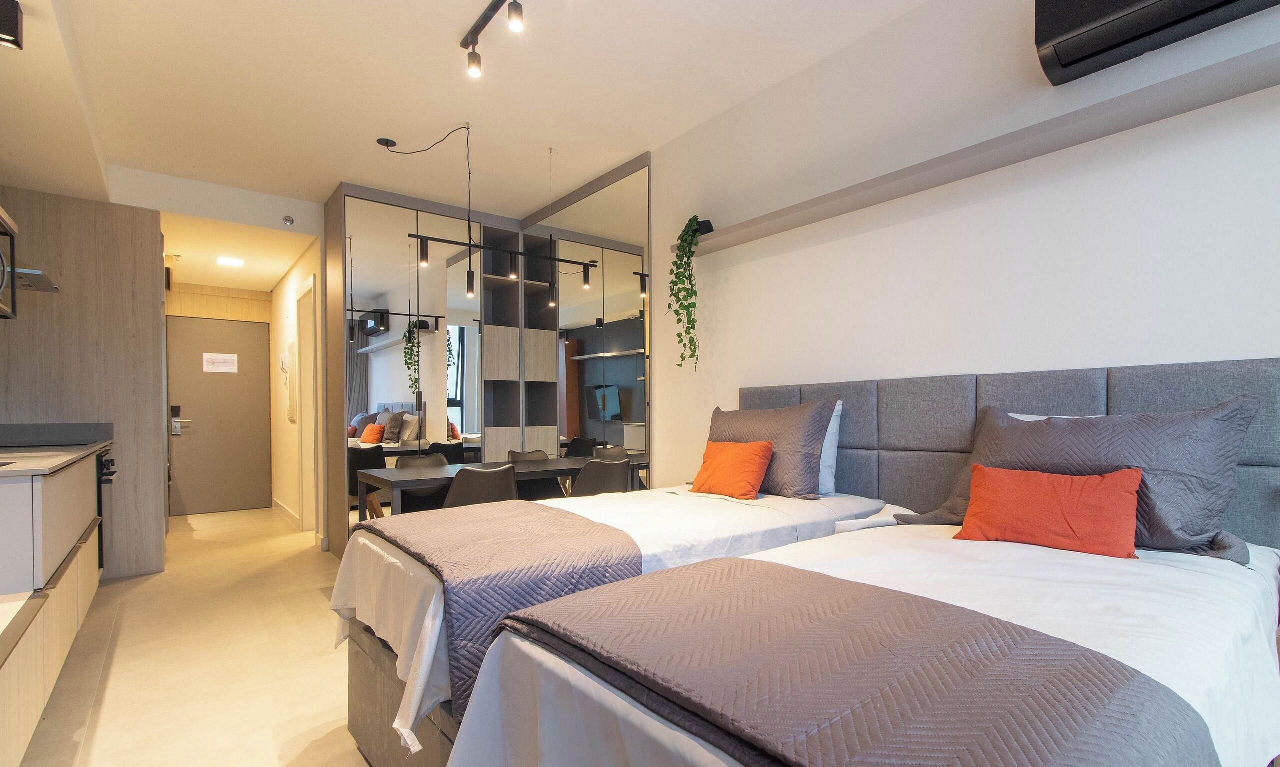 Een moderne hotelkamer met twee bedden, een bureau, een spiegel en een hangplant.