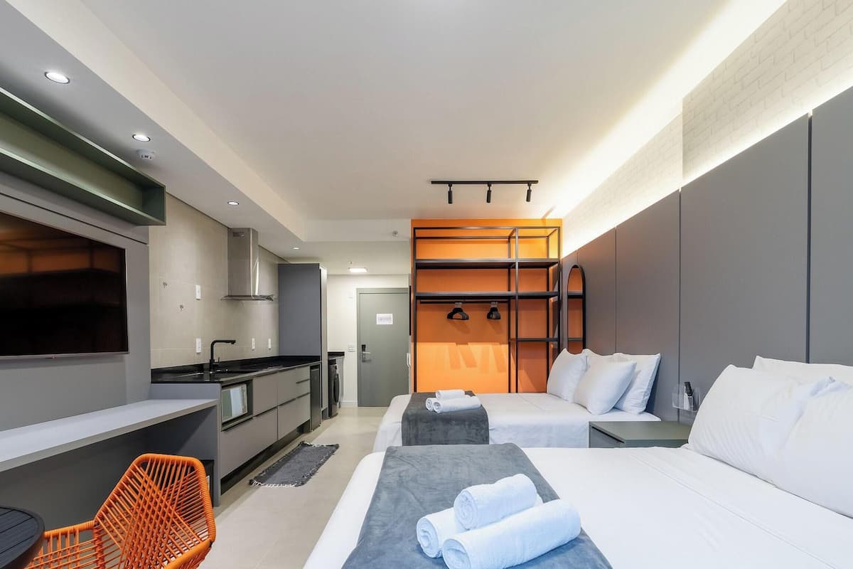 A modern hotel room with a kitchenette, two beds, a TV, and a seating area.