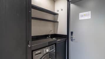 A compact laundry room with a washing machine, a sink, and a shelf.
