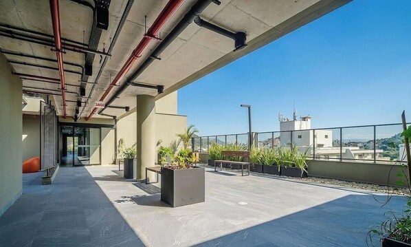 An outdoor terrace with a concrete floor, potted plants, and a view of the city. - Modern and Fully Equipped Apartments Just Minutes From Lagoa da Conceicao and the Beach - VTD (Florianópolis)