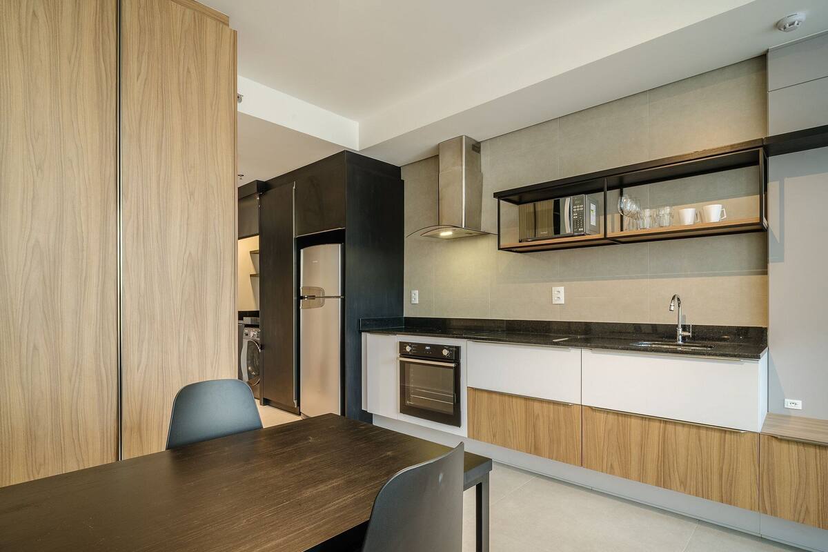 A modern kitchen with built-in appliances, a dining area with a wooden table, and a view of the adjacent living space.