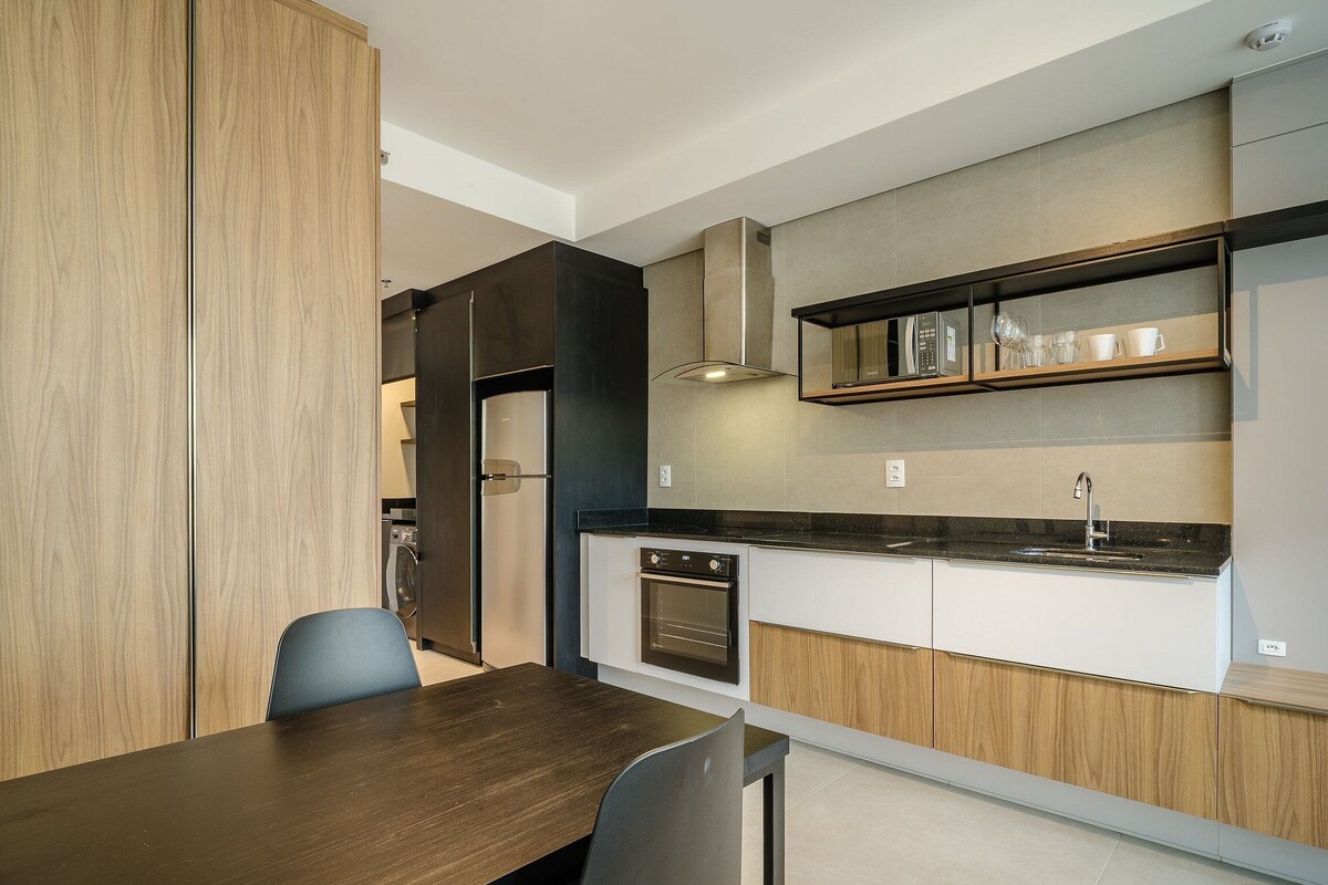 A modern kitchen with built-in appliances, a dining area with a wooden table, and a view of the adjacent living space.