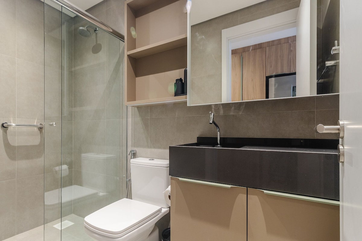 A modern bathroom with a glass shower enclosure, a white toilet, and a black sink with a mirror above.