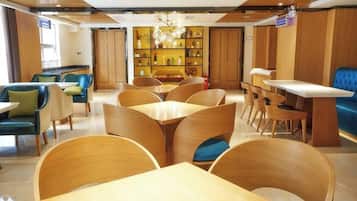 Een hotel lobby met houten meubilair, een kroonluchter in het midden en een zithoek met blauwe stoelen.