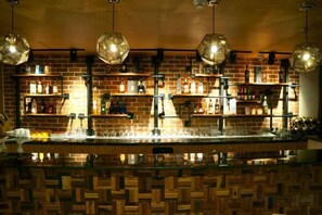 Un espace bar avec des murs en briques, des étagères remplies de bouteilles et des luminaires suspendus.