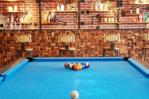 A pool table with a ball, surrounded by chairs, in a room with a brick wall and shelves with bottles. - M-one Hotel (Guiyang)