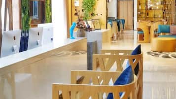 A hotel reception area with a reception desk, wooden chairs, and a seating area with a patterned rug.