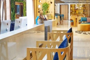 Un espace d’accueil d’hôtel comprenant un comptoir de réception, des chaises en bois et un coin salon agrémenté d’un tapis à motifs.