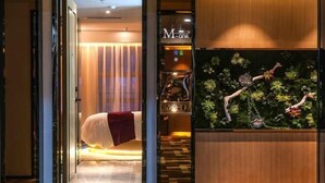 A hotel room with a bed, a reception desk, and a wall with a plant display. - M-one Hotel (Guiyang)