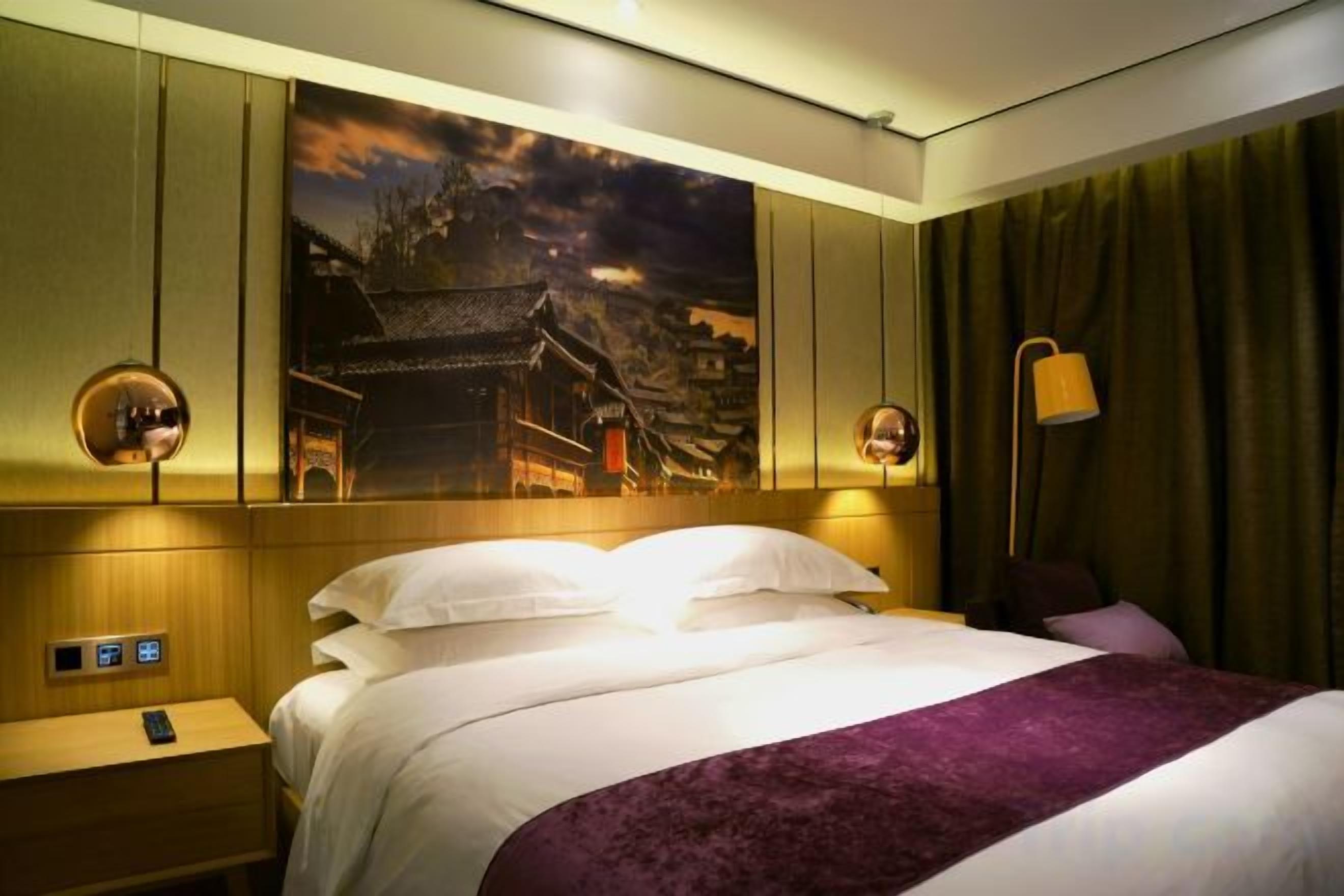 A hotel room with a large bed, a nightstand, a wall-mounted lamp, and a painting.